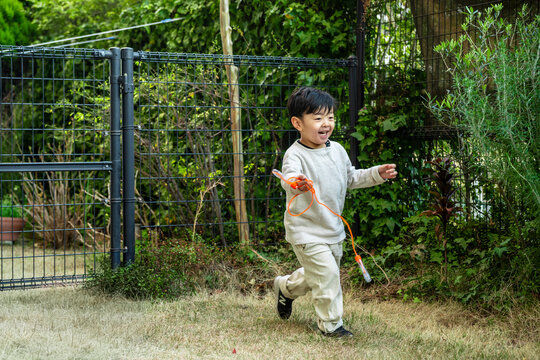 A young boy running joyfully with a jump rope in a sunny outdoor yard.