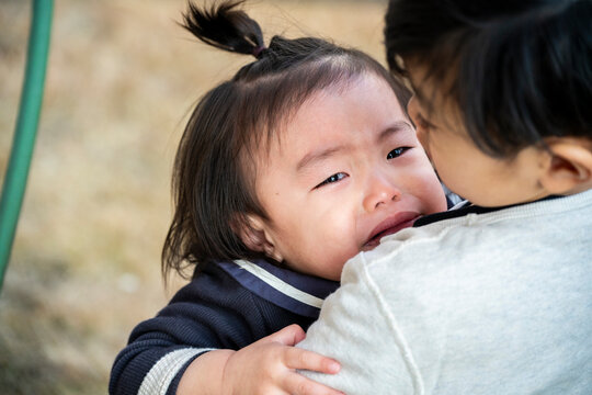 Close-up of a crying toddler with a ponytail being held outdoors.