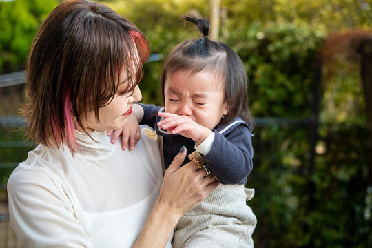 A mother gently comforting and consoling her crying toddler outdoors.