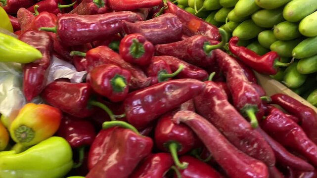Bell peppers and cucumbers being offered for sale, high-angle close-up of red, yellow and green vegetables piled in adjacent market bins, showcasing produce merchandising and cooking ingredients