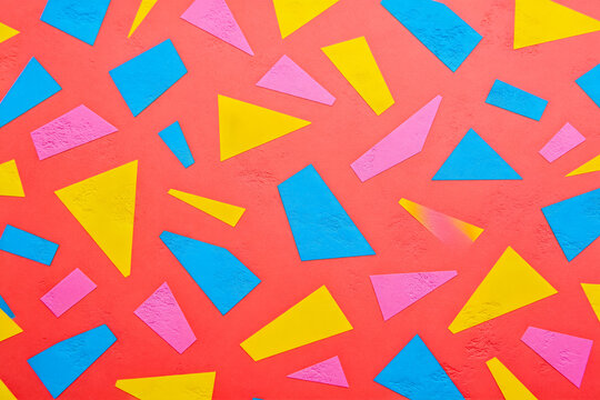 A vibrant repeating geometric pattern with pink, blue, yellow shapes on a coral textured background, for design use.