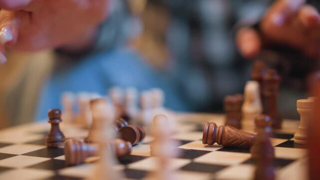 Close up of two people playing chess with wooden pieces on checkered board hands moving pawns and capturing opponent piece. Chessboard details include black white squares background blurred