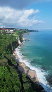 Coastal wave scene. Serene emerald waters crashing against rugged cliffs from above. Stunning aerial perspective capturing foaming waves and jagged coastline dynamics, Jimbaran, Bali, vertical video
