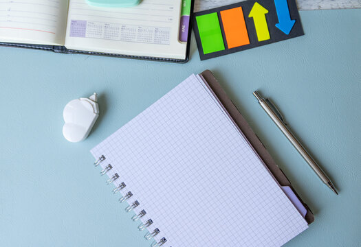 Blank spiral notebook with pen, arrow flags and cloud-shaped correction tool on pastel blue.