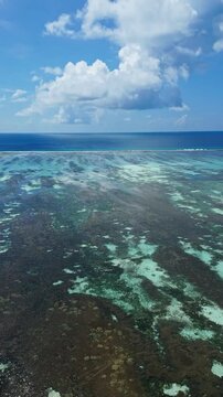 Transparent turquoise lagoon reveals sandy bottom and coral patches, while small boats travel across calm shallow water under a bright sunny blue sky in Maldives.Vertical video