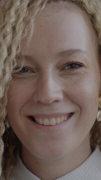 Close-up slow motion portrait of joyful young woman playing with long curly hair smiling looking at camera. People and individual style concept.