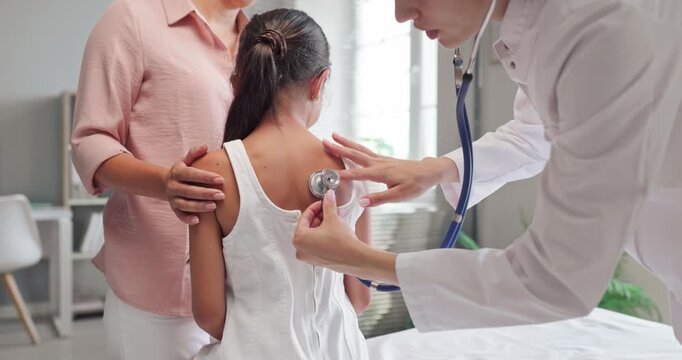 Doctor listens to child with stethoscope mother near. Pediatrician guides examination in consultation at clinic, checking lungs for diagnosis. Family healthcare concept of diagnosis.