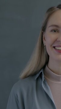 Slow motion portrait of charming young lady waving hand smiling on gray background. Hello gesture and friendly people concept.