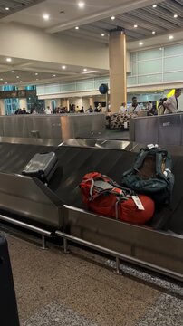 Baggage claim area in an airport with luggage on the conveyor belt. Travelers are waiting in the background for their bags.