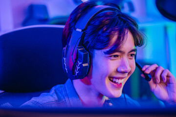 Close up of cheerful Asian man gamer talking into headset microphone while playing online game © SpaceOak