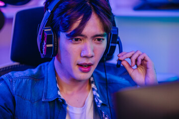 Close up of cheerful Asian man gamer talking into headset microphone while playing online game © SpaceOak