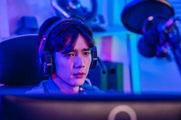 Close up of cheerful Asian man gamer talking into headset microphone while playing online game © SpaceOak