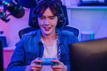 Happy Asian man gamer in headset holding gamepad and playing video game in neon gaming room © SpaceOak