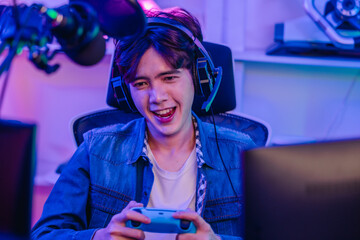 Happy Asian man gamer in headset holding gamepad and playing video game in neon gaming room © SpaceOak