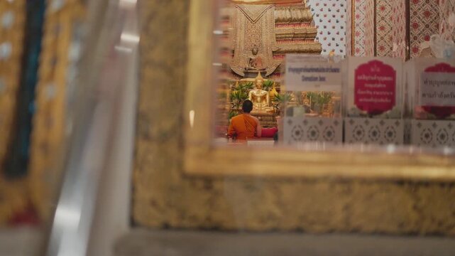 Reflection of a monk in orange robes praying and meditating in a tranquil thai temple