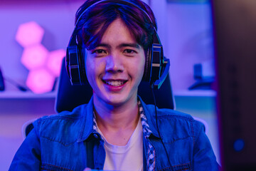 Happy Asian man gamer in headset holding gamepad and playing video game in neon gaming room © SpaceOak