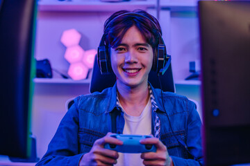 Happy Asian man gamer in headset holding gamepad and playing video game in neon gaming room © SpaceOak