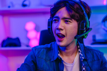 Excited Asian man gamer in headset shouting and laughing while playing video game at home © SpaceOak