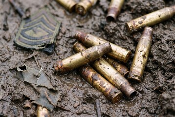 Obraz premium Spent bullet casings and a military rank insignia lie discarded in muddy ground, evoking a sense of conflict and its aftermath.