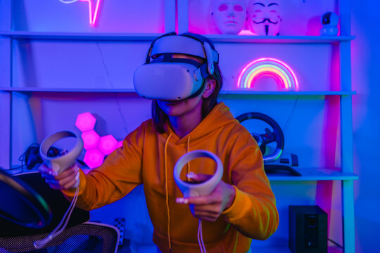 Young woman wearing VR headset and holding controllers playing virtual reality game at home