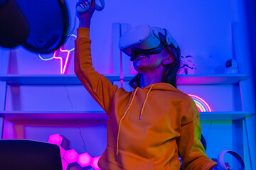 Excited woman in VR headset raising arms with controllers while playing virtual reality game © SpaceOak