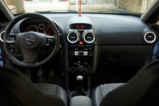 Opel brand logo on the steering wheel inside the driver cabin of a modern Corsa passenger car featuring the center console radio interface dashboard and gear shift.