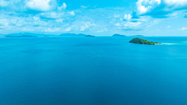 Panoramic aerial view of a lush green tropical island in the middle of a vast blue ocean under a bright sky with clouds, representing vacation, travel, and scenic nature.concept travel	