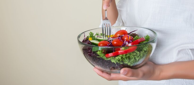 Woman holding bowl of fresh vegetable salad with fork, healthy eating and diet concept