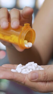 close up woman hand holding a medicine, with pours the pills out of the yellow orange medicine bottle. Stop drug use Taking Medication Caring for the health care medical concept.
