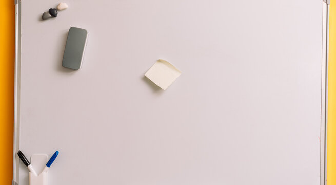 Blank sticky note on a whiteboard with magnets and an eraser with curled upper edge.