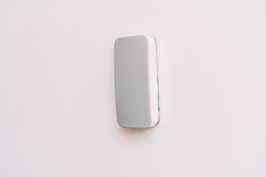Gray rectangular eraser attached to a whiteboard with a white edge.