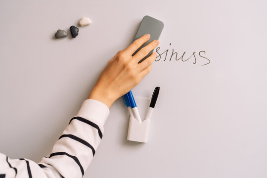 Hand erasing black lettering above a whiteboard marker holder with a gray eraser.