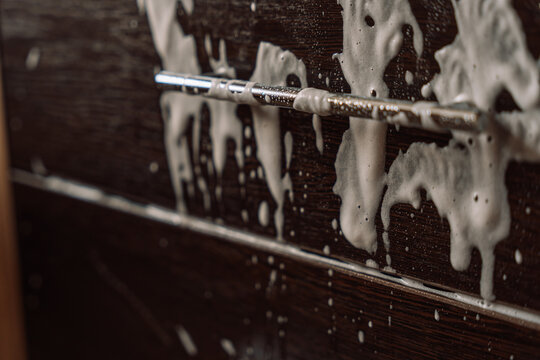 Cleaning foam dripping around a metal drawer handle on dark woodgrain furniture.
