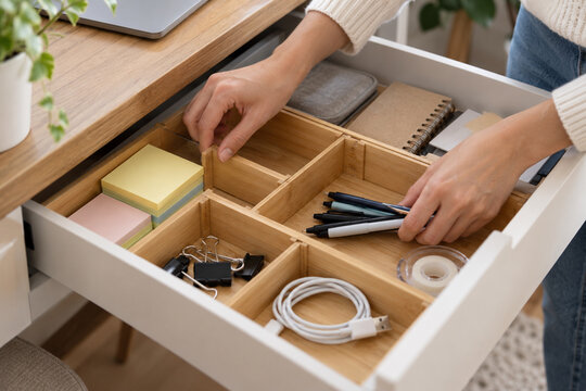 Hands arranging office supplies in an adjustable desk drawer organizer