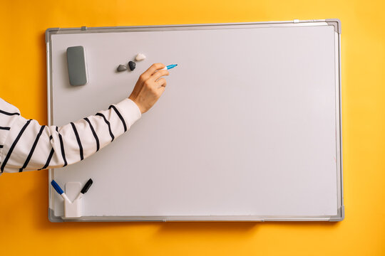 Hand holding an uncapped blue marker before a blank whiteboard beside three small magnets.