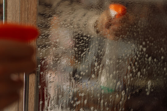 Hand holding a spray nozzle before a foam-covered mirror with a reflected bottle.