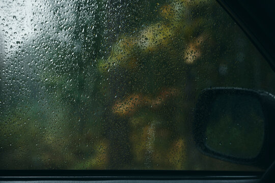 Raindrops on a car side window with blurred autumn foliage