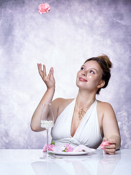 Woman in white dress admires a pink carnation flower tossed into the air with delighted expression.