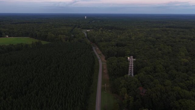 Sold land planned for a data center in Louisa County, Virginia, remains wooded, with a rural road and communications tower crossing the view. Aerial drone wide shot