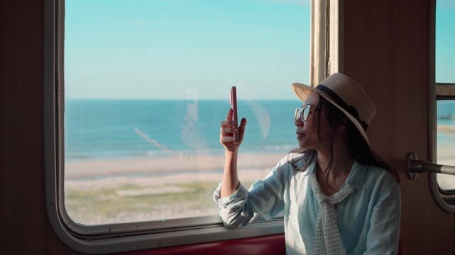 Young female traveler taking photos and enjoying the sea view while traveling by train during her summer vacation