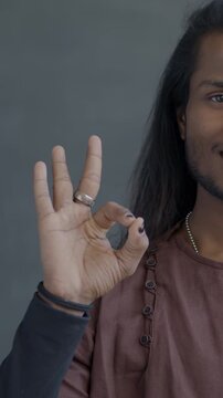 Portrait of Indian man in traditional clothes showing OK hand gesture smiling looking at camera on black background. People and positive emotion concept.