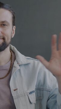 Slow motion portrait of happy young man waving hand smiling looking at camera on black studio background. People and nonverbal communication concept.