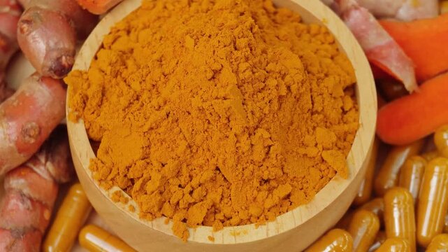 Turmeric powder in wooden bowl surrounded by herbal capsules and fresh curcuma roots