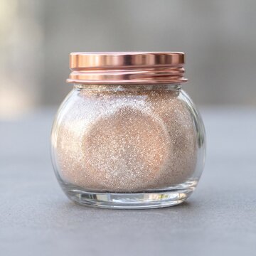 Jar of rose gold shimmer pigment powder in a glass container with copper lid for cosmetic swatch background and beauty product styling