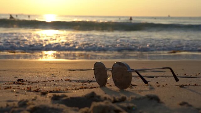 A serene beach sunset with stylish sunglasses resting on golden sand, reflecting the beauty of nature and the tranquility of the ocean waves lapping at the shore.