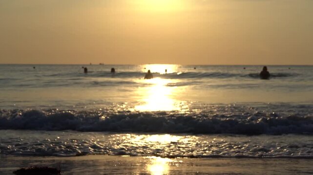 A Serene Sunset Over Calm Ocean Waters: Captivating Waves Reflecting Golden Sunlight While Surfers Enjoy the Tranquility of the Distant Horizon