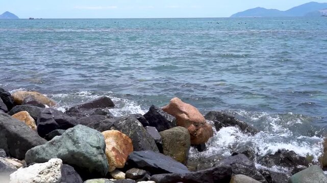 Serene Coastal View Featuring Colorful Rocks Along the Shoreline with Gentle Waves Lapping at the Edge of a Vibrant Seascape Under a Clear Sky