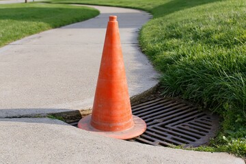 Obraz premium The Orange Traffic Cone Guarding a Street Drain on a Sunny Sidewalk