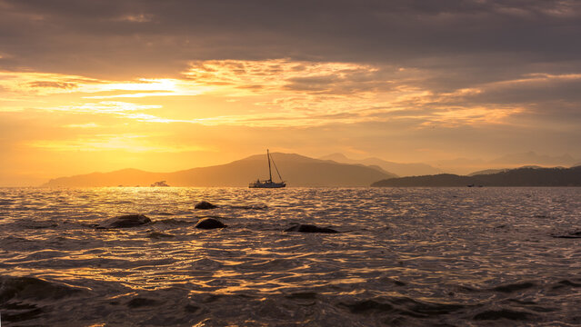 Sailboat on calm water at golden sunset with mountains on the horizon, Vancouver, British Columbia, Canada