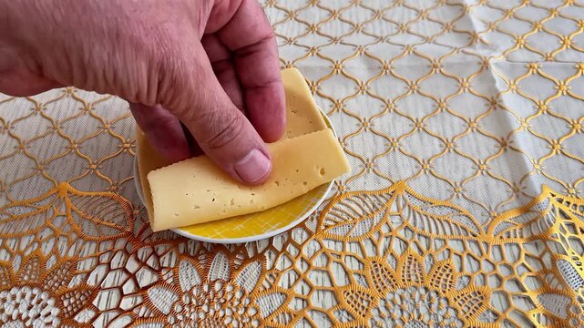 A hand places a folded slice of yellow cheese on a decorative plate over an elegant handmade crochet tablecloth, creating a simple traditional food setting with rustic charm